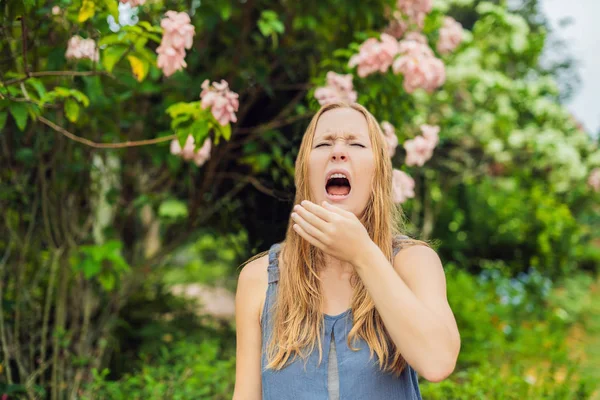 Ung vacker kvinna som blåser näsa framför blommande träd. Vårens allergikoncept — Stockfoto