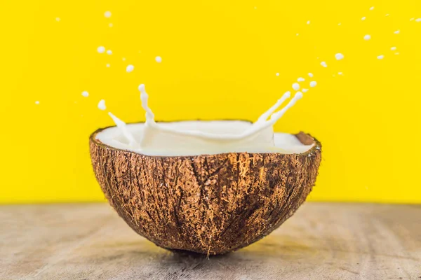 Coconut fruit and milk splash inside it on yellow background