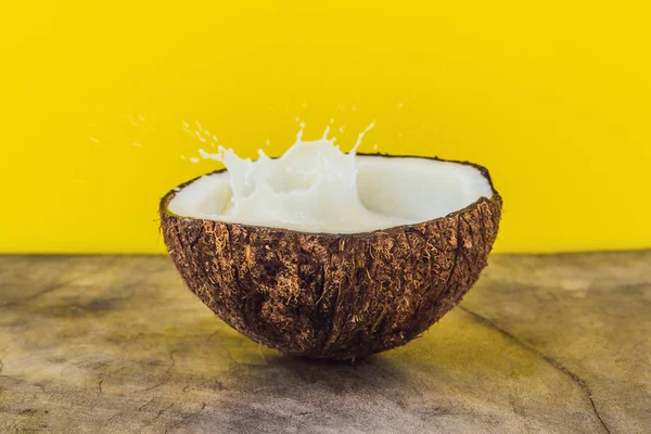 Coconut fruit and milk splash inside it on yellow background