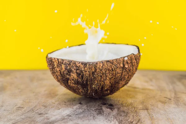 Coconut fruit and milk splash inside it on yellow background