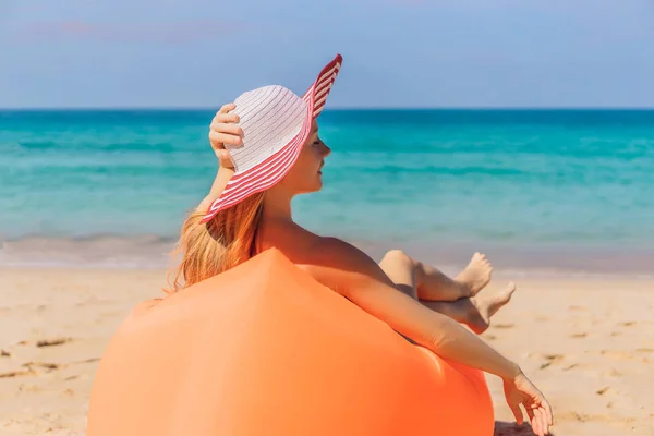 Retrato de estilo de vida de verano de una chica bonita sentada en el sofá inflable naranja en la playa de la isla tropical. Relajarse y disfrutar de la vida en la cama de aire —  Fotos de Stock