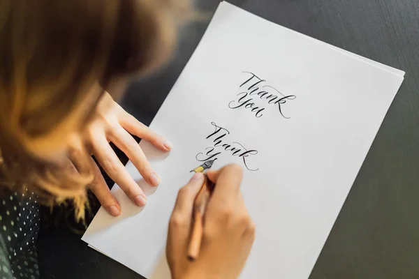 Les mains du calligraphe écrivent des phrases sur du papier blanc. Phrase - Merci. Inscrire des lettres ornementales décorées. Calligraphie, graphisme, lettrage, écriture, concept de création — Photo