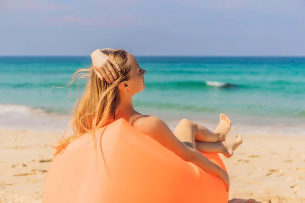 Retrato de estilo de vida de verano de una chica bonita sentada en el sofá inflable naranja en la playa de la isla tropical. Relajarse y disfrutar de la vida en la cama de aire —  Fotos de Stock