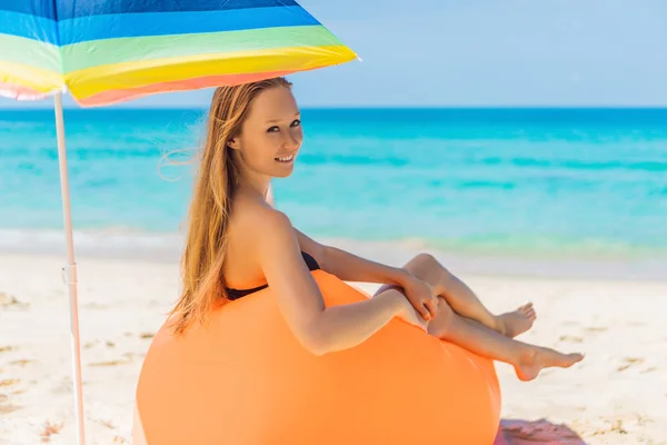 Summer lifestyle portrait of pretty girl sitting on the orange inflatable sofa on the beach of tropical island. Relaxing and enjoying life on air bed — Stock Photo, Image