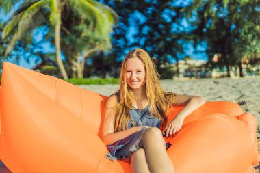 Yaz yaşam tarzı tropik ada plaj turuncu şişme kanepede oturan güzel kız portresi. Rahatlatıcı ve hayat hava yatakta zevk