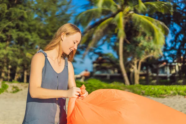 Retrato de estilo de vida de verano de mujer infla un sofá naranja inflable en la playa de la isla tropical. Relajarse y disfrutar de la vida en la cama de aire —  Fotos de Stock