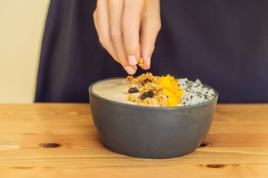 Kadın aşçılar güler yüzlü kase yapılmış mango, muz, granola, rendelenmiş hindistan cevizi, dragon meyve, chia tohum ve ahşap zemin üzerine nane. Kavram meyve, vitaminler