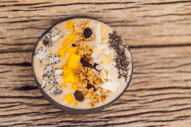 Mango, muz, granola, rendelenmiş hindistan cevizi, ejderha meyvesi, chia tohumu ve ahşap arkaplanda naneden yapılmış meyve suyu kaseleri. Meyve, vitamin kavramları