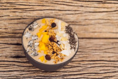 Mango, muz, granola, rendelenmiş hindistan cevizi, ejderha meyvesi, chia tohumu ve ahşap arkaplanda naneden yapılmış meyve suyu kaseleri. Meyve, vitamin kavramları