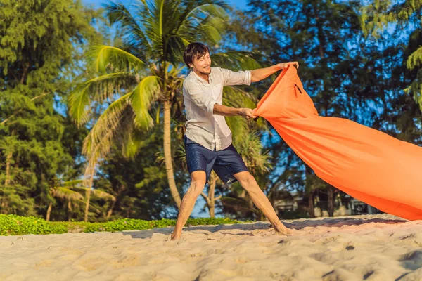 Stile di vita estivo ritratto dell'uomo gonfia un divano gonfiabile arancione sulla spiaggia dell'isola tropicale. Rilassante e godersi la vita sul letto ad aria — Foto Stock