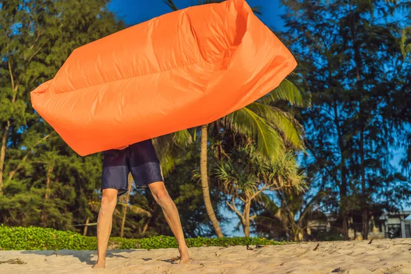 Zomer levensstijl portret van man opgeblazen een opblaasbare oranje Bank op het strand van het tropische eiland. Ontspannen en genieten van het leven op lucht bed — Stockfoto