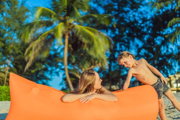 Stile di vita estivo ritratto di madre e figlio seduti sul divano gonfiabile arancione sulla spiaggia dell'isola tropicale. Rilassante e godersi la vita sul letto ad aria — Foto Stock