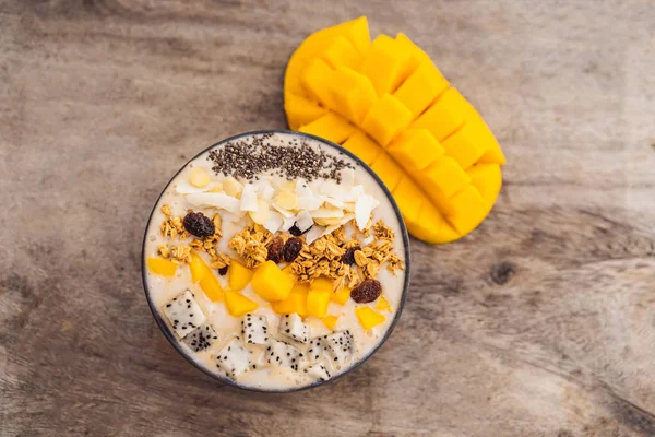 Smoothie bowls made with mango, banana, granola, grated coconut, dragon fruit, chia seeds and mint on wooden background. Concept fruits, vitamins