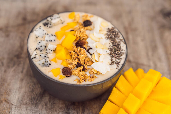 Smoothie bowls made with mango, banana, granola, grated coconut, dragon fruit, chia seeds and mint on wooden background. Concept fruits, vitamins