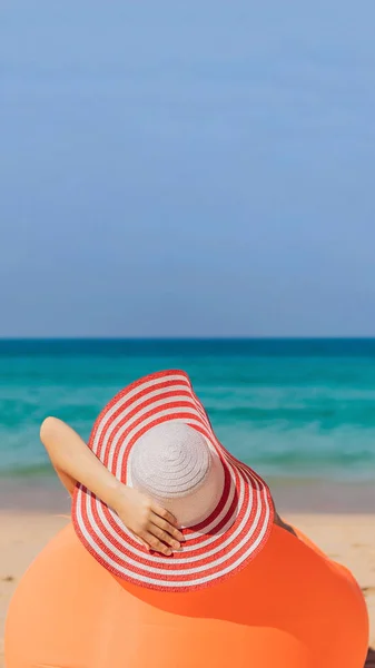 Retrato de estilo de vida de verano de una chica bonita sentada en el sofá inflable naranja en la playa de la isla tropical. Relajarse y disfrutar de la vida en la cama de aire FORMATO VERTICAL para Instagram historia móvil o — Foto de Stock