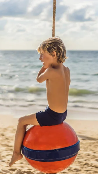 Un garçon en balançoire sur la plage. Maman et son fils passent du temps sur la plage FORMAT VERTICAL pour Instagram histoire mobile ou la taille des histoires. Papier peint mobile — Photo