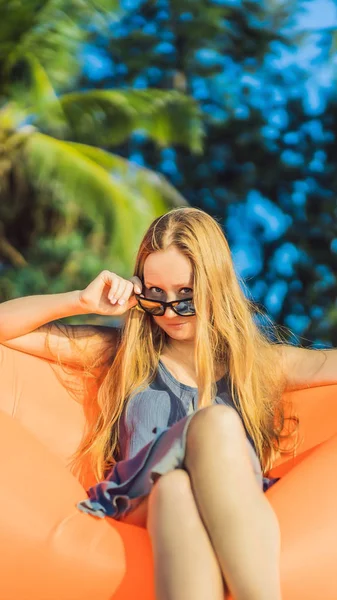 Nyári életmód portréja a csinos lány ül a narancssárga felfújható kanapé szigetén a tengerparton. Pihenés, és élvezi az élet, a levegő ágy függőleges formátum Instagram mobil történet vagy — Stock Fotó