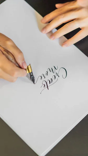 Calígrafo manos escribe frase en papel blanco. Frase - Crear más. Inscribiendo letras ornamentales decoradas. Caligrafía, diseño gráfico, letras, escritura a mano, concepto de creación FORMATO VERTICAL — Foto de Stock