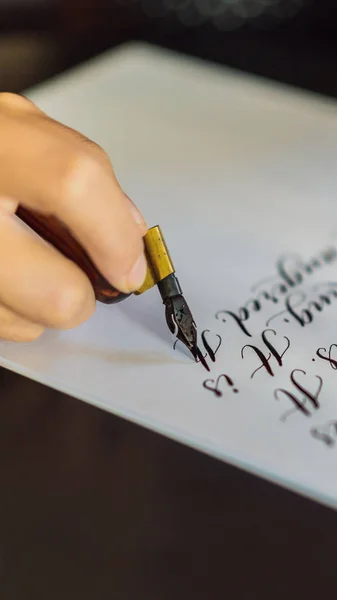 Calígrafo manos escribe frase en papel blanco. Frase bíblica sobre el amor Inscripción de letras ornamentales decoradas. Caligrafía, diseño gráfico, letras, escritura a mano, concepto de creación FORMATO VERTICAL —  Fotos de Stock