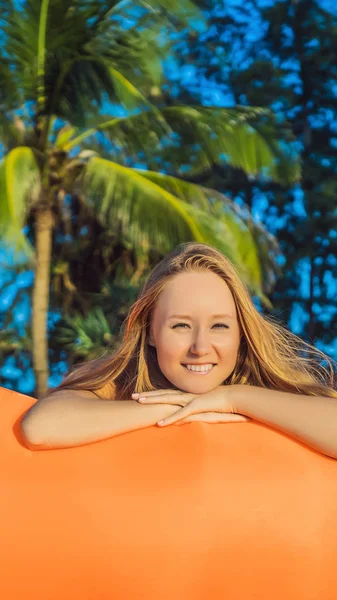 Summer lifestyle portrait of pretty girl sitting on the orange inflatable sofa on the beach of tropical island. Relaxing and enjoying life on air bed VERTICAL FORMAT for Instagram mobile story or — Stock Photo, Image