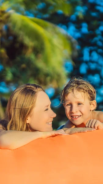 Estilo de vida de verão retrato de mãe e filho sentado no sofá inflável laranja na praia da ilha tropical. Relaxar e desfrutar da vida na cama de ar FORMATO VERTICAL para Instagram história móvel ou — Fotografia de Stock