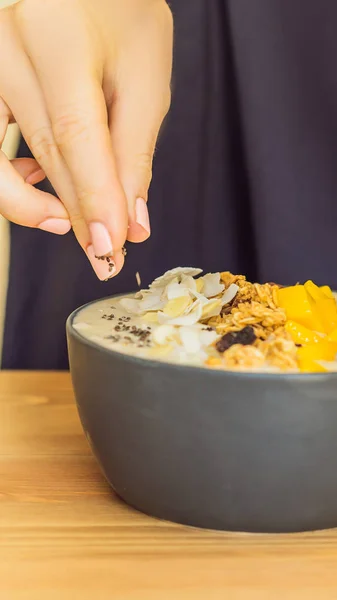 Vrouw koks smoothie kommen gemaakt met mango, banaan, muesli, geraspte kokos, dragon fruit, chia zaden en mint op houten achtergrond. Concept vruchten, vitaminen verticale indeling voor mobiele verhaal van Instagram — Stockfoto