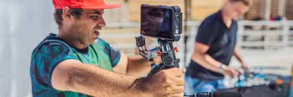 A equipe de produção em uma filmagem de vídeo comercial. O operador Steadicam usa o estabilizador de câmera de 3 eixos e a câmera de grau de cinema BANNER, LONG FORMAT — Fotografia de Stock