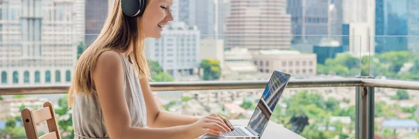 Молодая женщина учит иностранный язык или учит иностранный язык в Интернете на своем балконе на фоне большого города. Школьный онлайн-стиль жизни BANNER, LONG FORMAT — стоковое фото