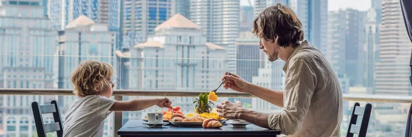 Famiglia felice che fa colazione sul balcone. Tavolino per la colazione con frutta e pane croisant su un balcone sullo sfondo della grande città BANNER, FORMATO LUNGO — Foto Stock