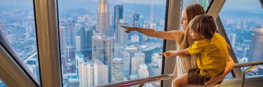 Anne ve oğlu Kuala lumpur cityscape arıyoruz. Gün batımı gökdelenler içinde Malaysia bina panoramik manzaraya Kuala Lumpur şehir manzarası akşam. Çocuklar konseptiyle afiş, uzun biçimde seyahat