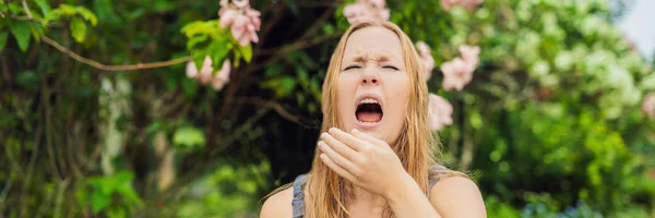 Young pretty woman blowing nose in front of blooming tree. Spring allergy concept BANNER, LONG FORMAT — Stock Photo, Image