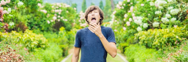 Young man blowing nose in front of blooming tree. Spring allergy concept BANNER, LONG FORMAT — Stock Photo, Image