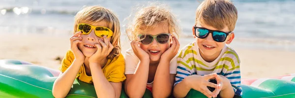 Tre bambini biondi con gli occhiali da sole sono sdraiati sulla spiaggia BANNER, FORMATO LUNGO — Foto Stock