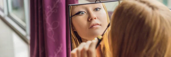 Mujer joven hace maquillaje sentado junto a la ventana con una vista panorámica de los rascacielos y la gran ciudad BANNER, FORMATO LARGO — Foto de Stock