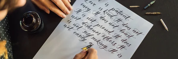 Les mains du calligraphe écrivent des phrases sur du papier blanc. Expression biblique sur l'amour Inscrire des lettres ornementales décorées. Calligraphie, graphisme, lettrage, écriture, concept de création BANNER, LONG — Photo