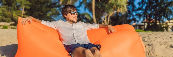 Estilo de vida de verão retrato do homem sentado no sofá inflável laranja na praia da ilha tropical. Relaxar e desfrutar da vida na cama de ar BANNER, LONG FORMAT — Fotografia de Stock
