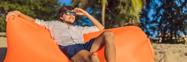 Estilo de vida de verão retrato do homem sentado no sofá inflável laranja na praia da ilha tropical. Relaxar e desfrutar da vida na cama de ar BANNER, LONG FORMAT — Fotografia de Stock