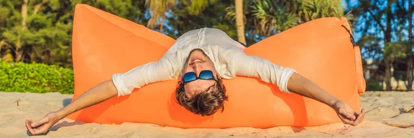 Zomer levensstijl portret van de man zit op de oranje opblaasbare bank op het strand van het tropische eiland. Ontspannen en genieten van het leven op lucht bed Banner, lange notatie — Stockfoto