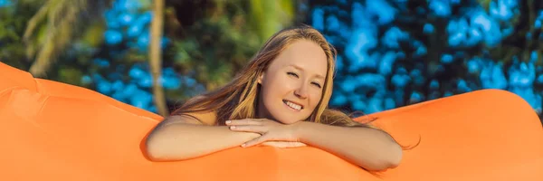 夏天生活方式的肖像漂亮的女孩坐在热带岛屿海滩上的橙色充气沙发上。放松和享受生活在空中床横幅, 长格式 — 图库照片