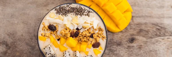 Smoothie bowls made with mango, banana, granola, grated coconut, dragon fruit, chia seeds and mint on wooden background. Concept fruits, vitamins BANNER, LONG FORMAT