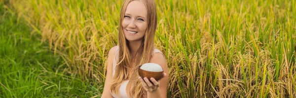 Bir kadın bir bardak haşlanmış pirinç bir olgun pirinç alan afiş, uzun biçimde arka planda ahşap bir fincan içinde tutuyor — Stok fotoğraf