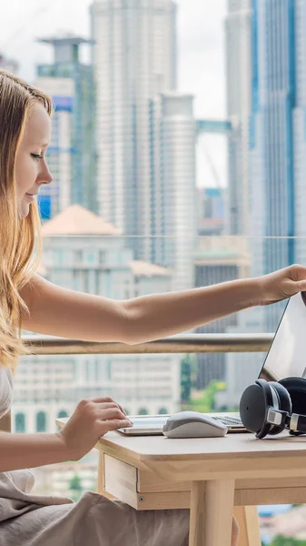 Jonge vrouw werkt aan een laptop op haar balkon met uitzicht op de wolkenkrabbers. Freelancer, het verre werk, werk van huis verticaal formaat voor Instagram mobiel verhaal of verhalen grootte. Mobiel behang — Stockfoto