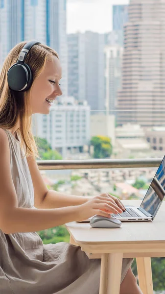 Ung kvinna undervisar ett främmande språk eller lär sig ett främmande språk på Internet på sin balkong mot bakgrund av en storstad. Online språk skola livsstil vertikalt format för Instagram — Stockfoto