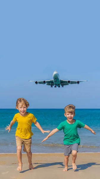 Dois meninos felizes se divertem na praia assistindo os aviões de pouso. Viajar em um avião com conceito de crianças. Espaço de texto. Ilha Phuket na Tailândia. Paraíso impressionante. Praia quente Mai Khao. Incrível. — Fotografia de Stock