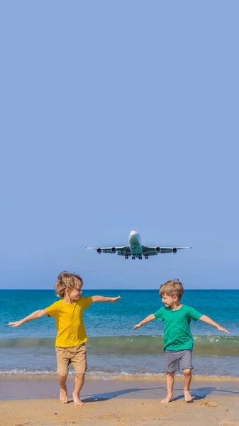 Due ragazzi felici si divertono sulla spiaggia a guardare gli aerei di atterraggio. Viaggiare su un aereo con il concetto di bambini. Spazio di testo. Island Phuket in Thailandia. Un paradiso impressionante. Spiaggia calda Mai Khao. Incredibile. — Foto Stock