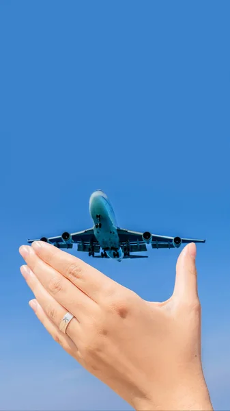 Mão feminina com um anel com um avião desenhado segurando um avião voando no céu. Viajando em um conceito de avião. Espaço de texto. Paraíso impressionante. Praia quente Mai Khao. Paisagem incrível FORMATO VERTICAL — Fotografia de Stock