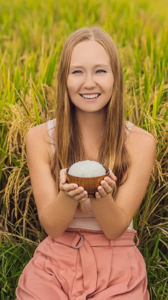 A woman is holding a cup of boiled rice in a wooden cup on the background of a ripe rice field VERTICAL FORMAT for Instagram mobile story or stories size. Mobile wallpaper — Stock Photo, Image