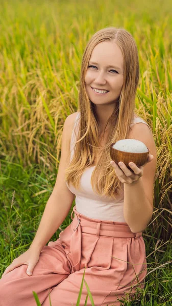 A woman is holding a cup of boiled rice in a wooden cup on the background of a ripe rice field VERTICAL FORMAT for Instagram mobile story or stories size. Mobile wallpaper — Stock Photo, Image