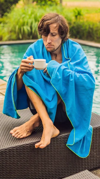 Sick man traveler. The man caught a cold on vacation, sits sad at the pool drinking tea and blows his nose into a napkin. His son is healthy and swimming in the pool. Travel insurance concept VERTICAL — Stock Photo, Image