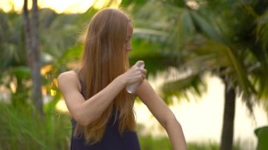 Güzel bir genç kadın bir ANTIMOSQUITO kovucu sprey derisinin üzerinde uygulama Superslowmotion vurdu. Tropikal bir arka plan. Sivrisinek savunma kavramı